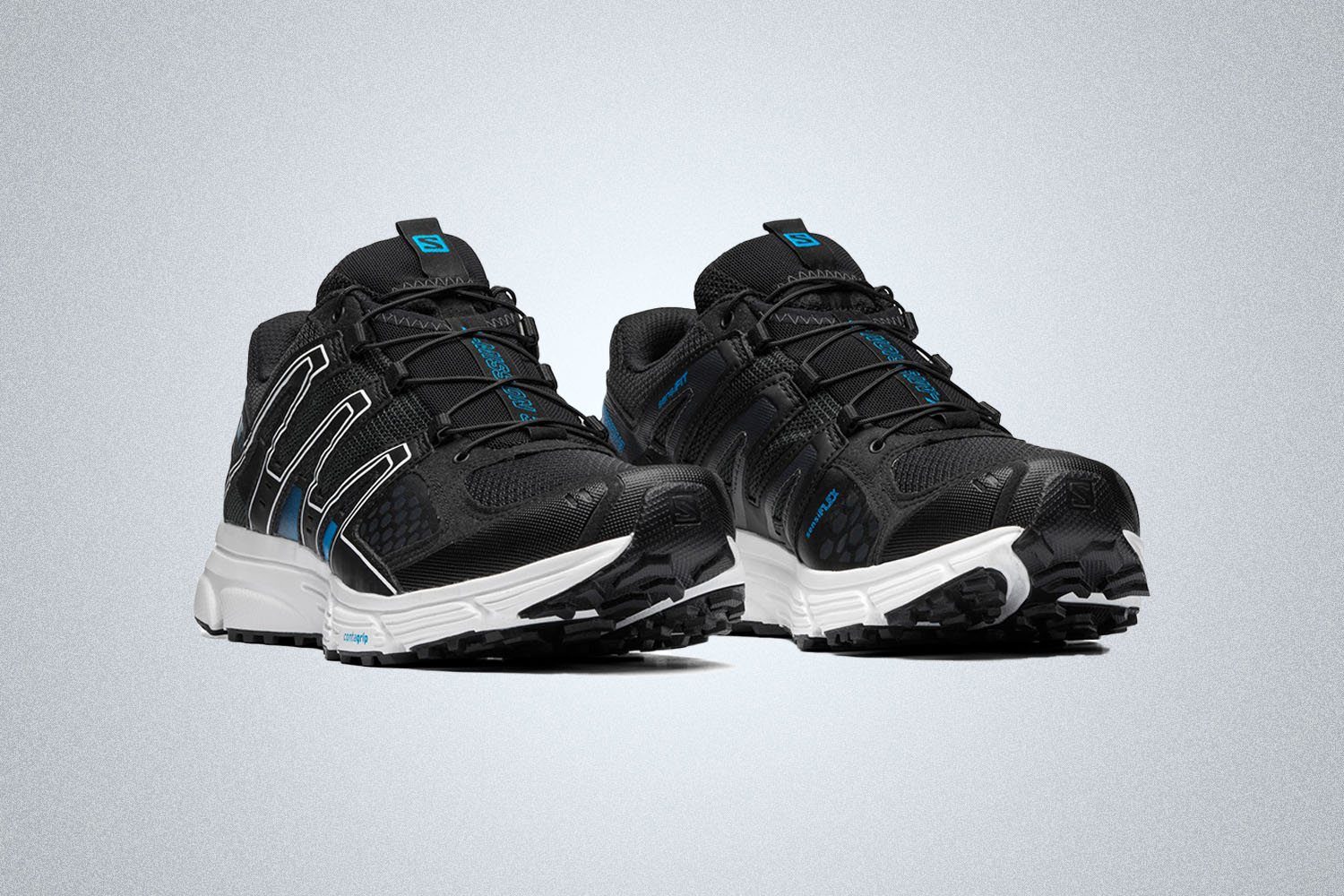 a pair of black Salomon hiking sneakers with white soles and blue accents on a grey background