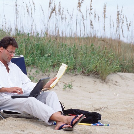 A man sitting with his laptop on the beach.