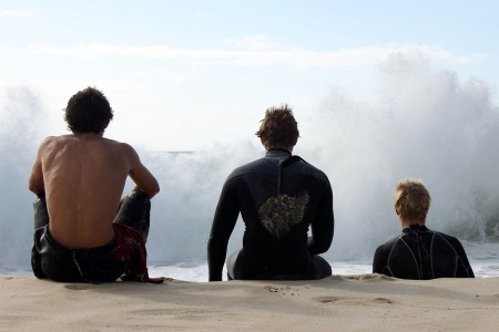 Three men sitting together on a beach.