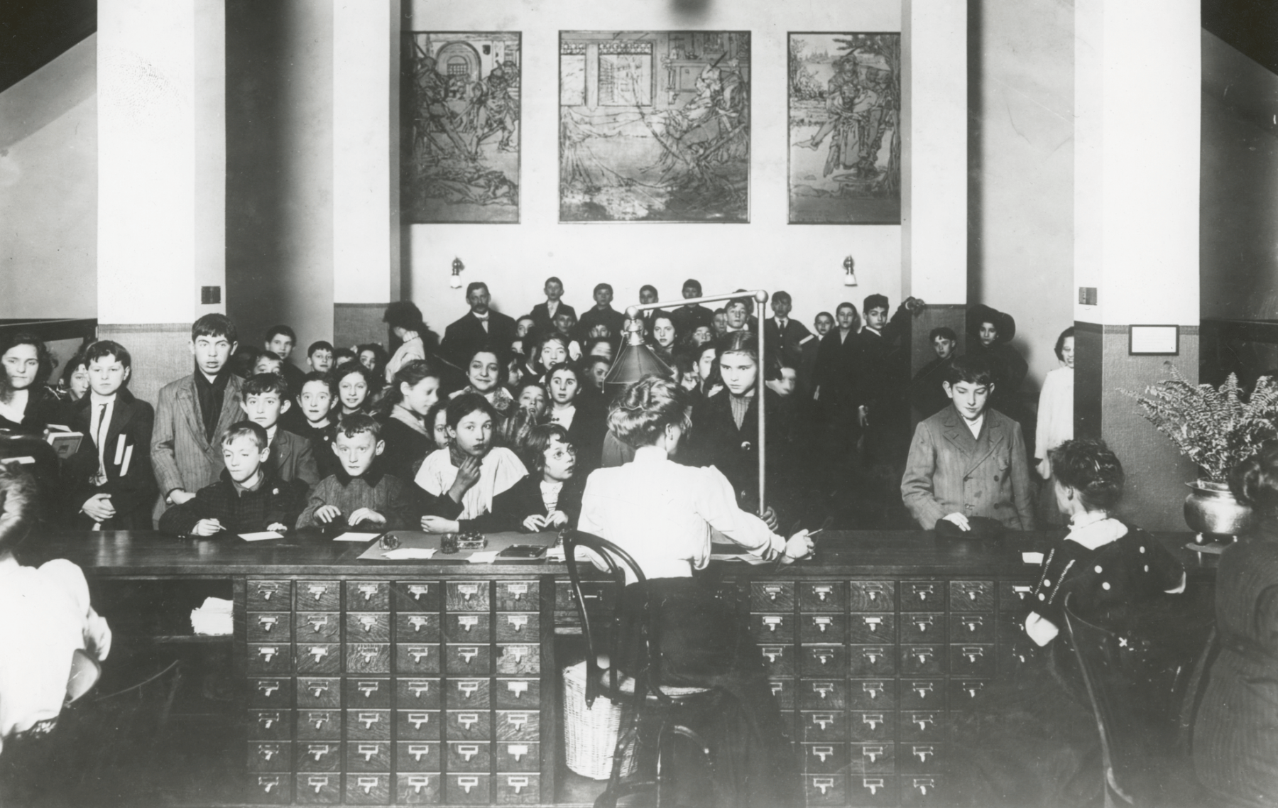 There are two points of interest here. One is the librarian at the desk confronted by the horde of children. There was an incredible readership and audience for the services these libraries produced or offered. The other thing you'll see is that she's sitting at a desk full of card catalogs. It's a stack of rows and rows of little drawers. Card catalogs were a really important key in analog technology. This picture shows the dual challenges of the library system. You see the kids eager for their books and the librarian with this giant desk of card catalogs. That was the technology she was using to manage the onslaught of patrons and the growing collection.