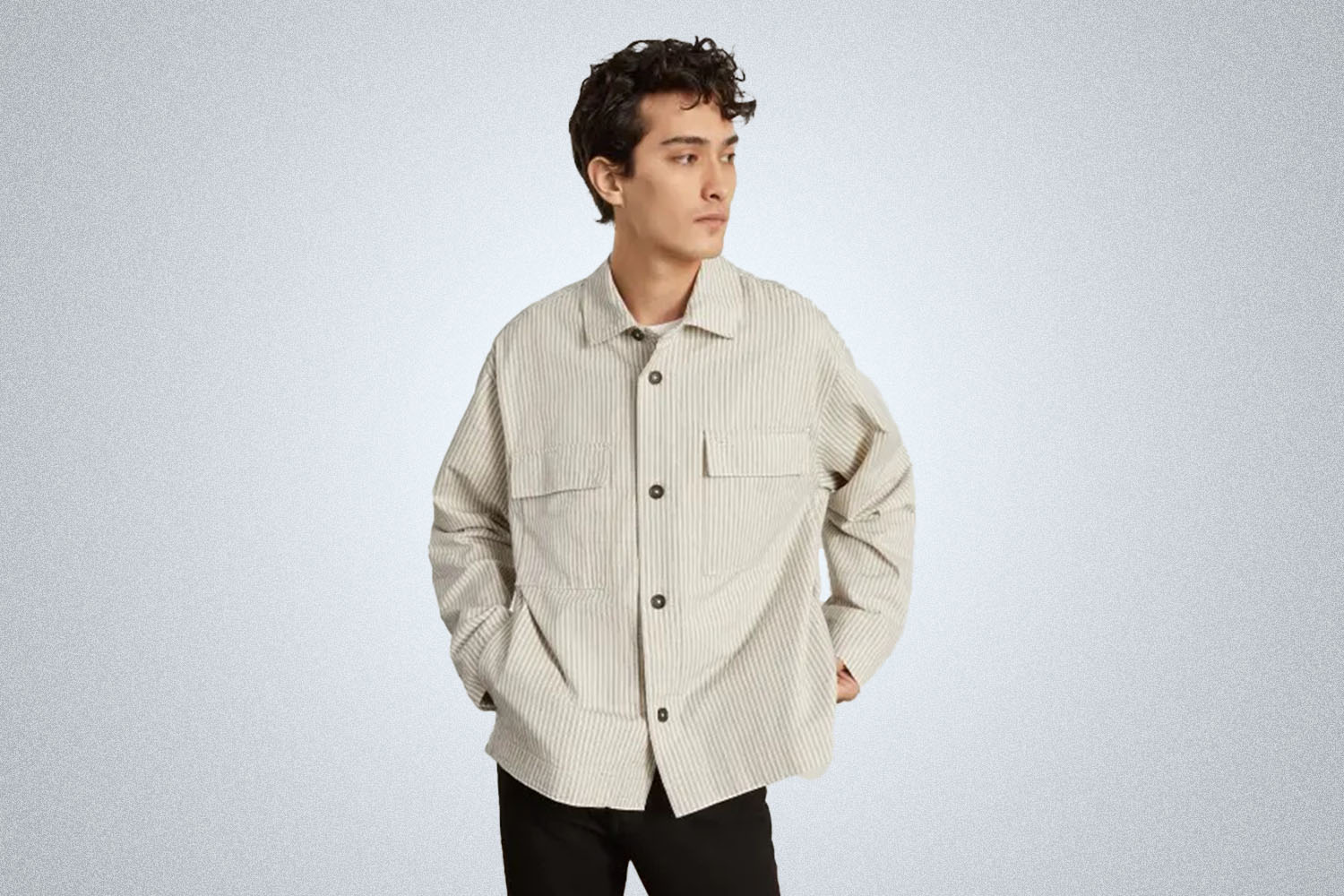 a model in a striped white jacket and black jeans from Everlane on a grey background