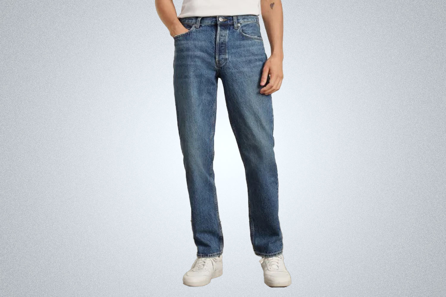 a model in a pair of medium wash Everlane jeans and a white tee on a grey background