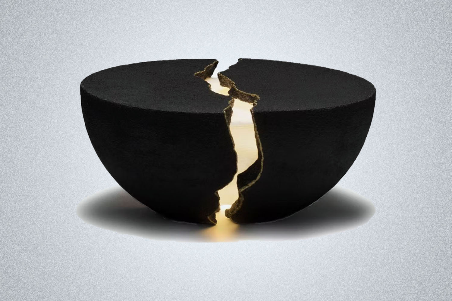 a black split apart speaker with a glowing gold center from Lumio on a grey background