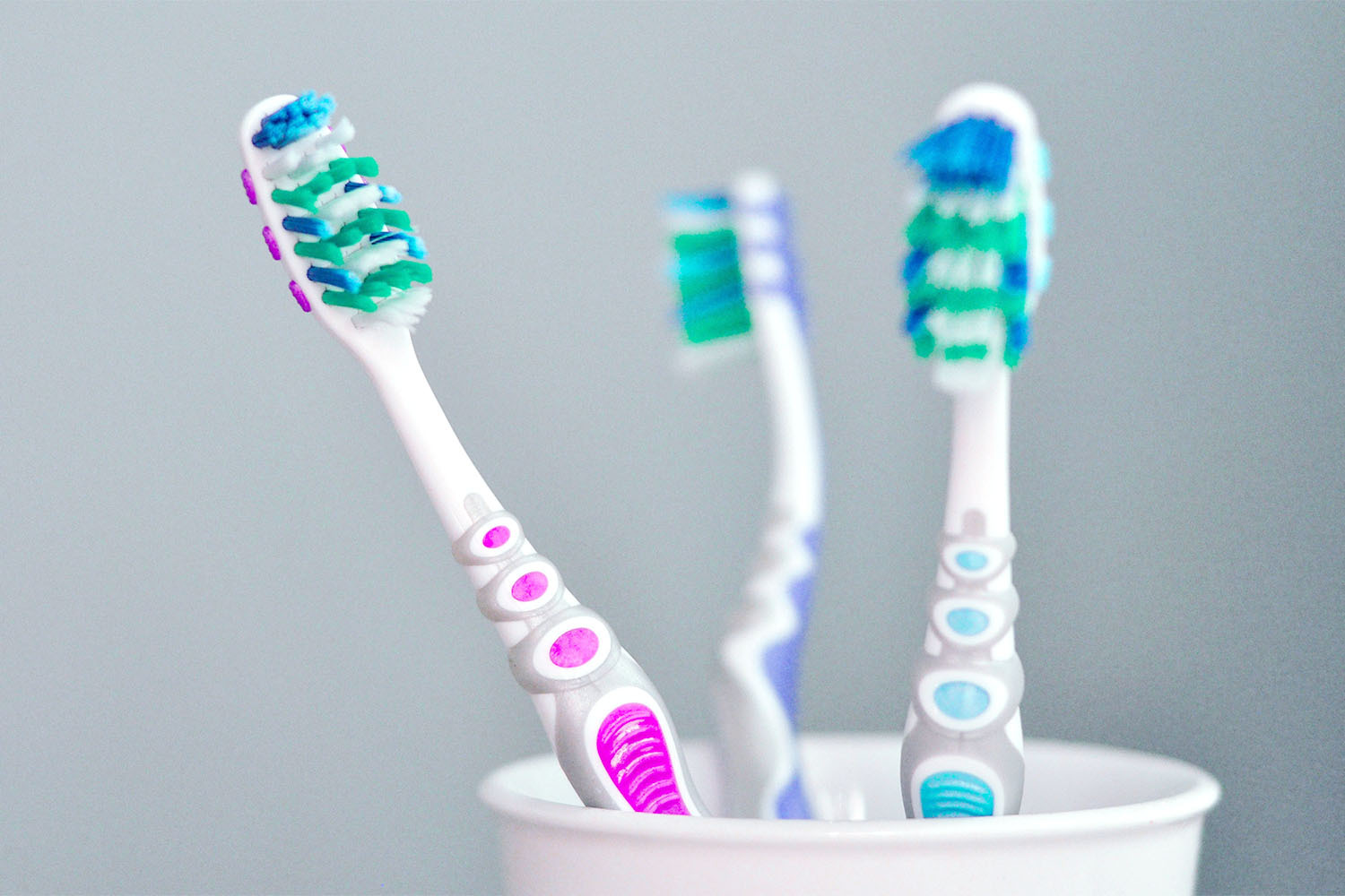 Close-up photo shows three toothbrushes in one white cup