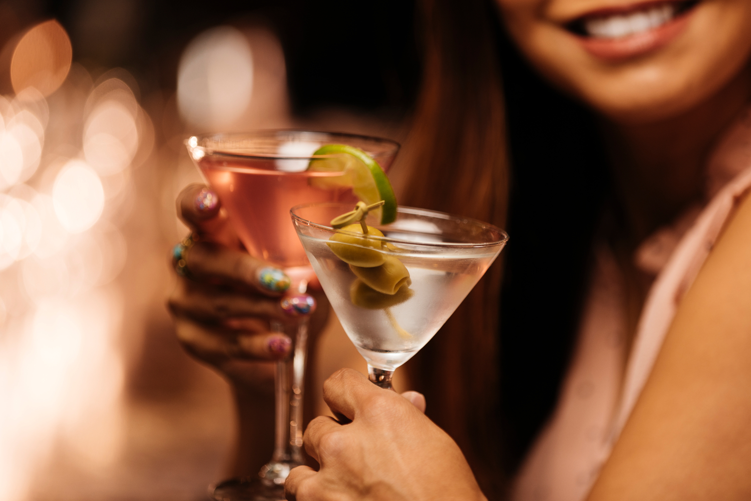 Close-up photo shows a couple clinking martini glasses on a date at a bar