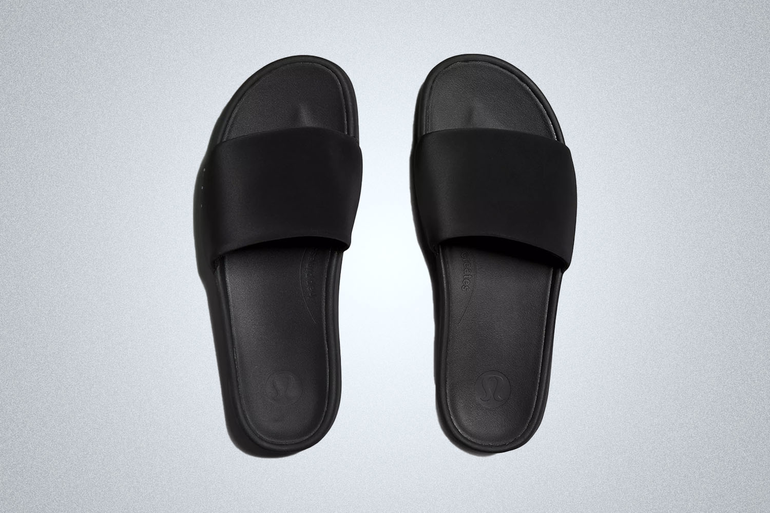 a pair of black lululemon sldies on a grey background