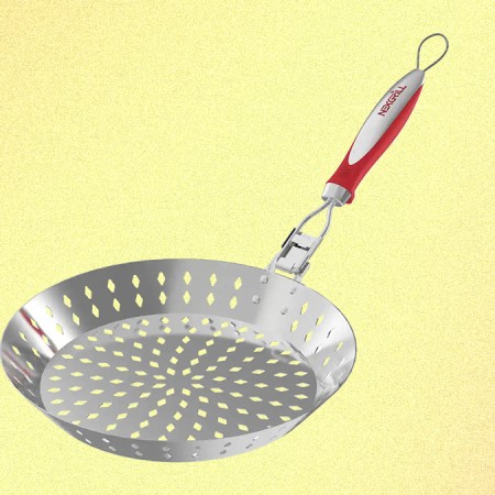 A grilling skillet from Nexgrill with a red handle and holes in the stainless steel basket, pictured on a yellow background.
