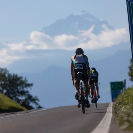 A man biking on a road in Switzerland with a mountain and clouds in the background