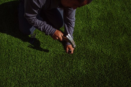 A man nails artificial turf down over a lawn. Here's why green synthetic lawns are catching on.
