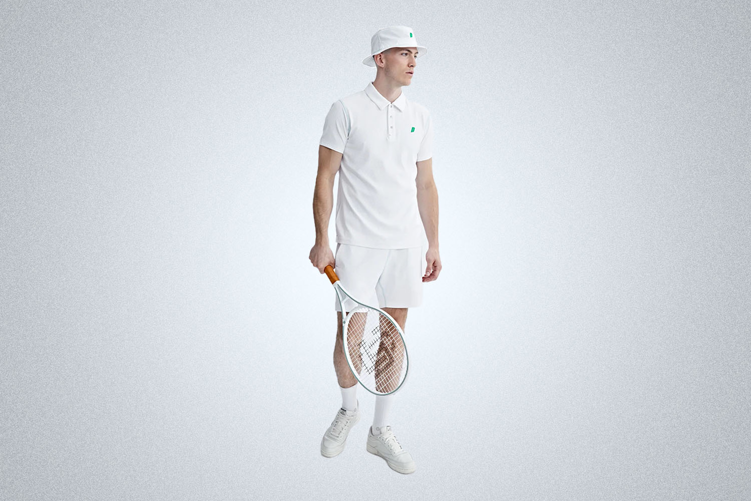 a model in the all-white reigning champ x prince collection, wearing a bucket hat, polo, shorts, and holding a tennis racket