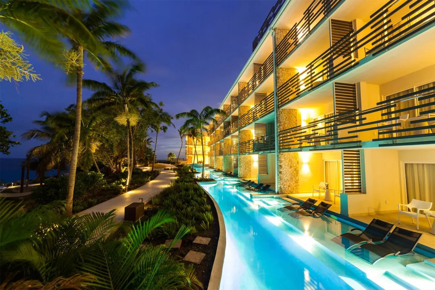 Sonesta Ocean Point Resort seen at night, with lights on in the rooms next to palm trees and a lit pool