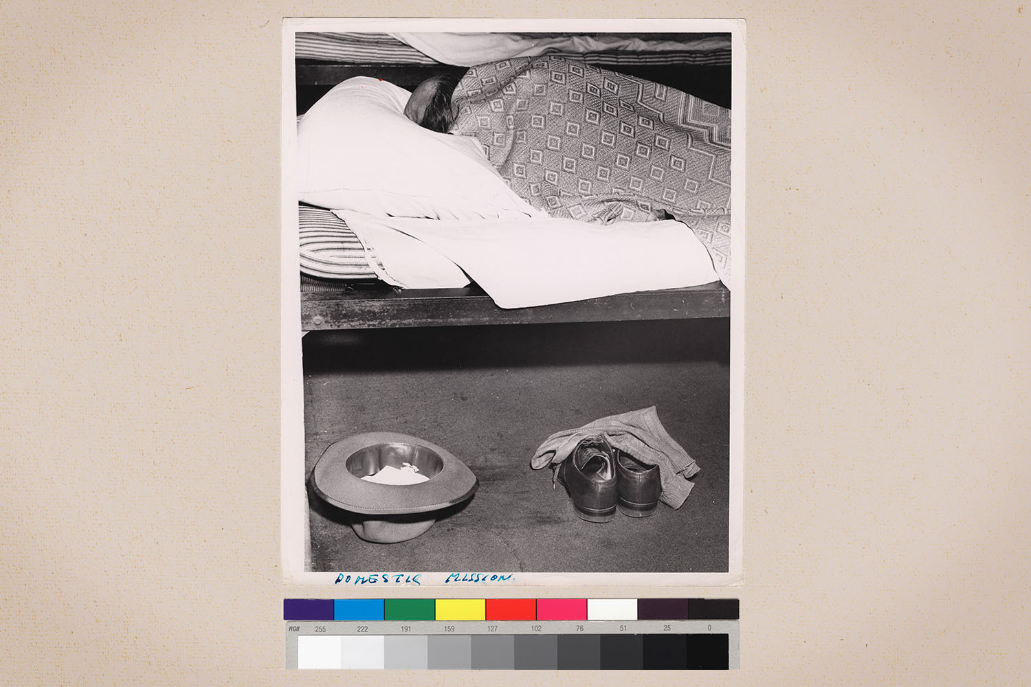 A man sleeping on a cot next to his shoes and hat on a beige background.