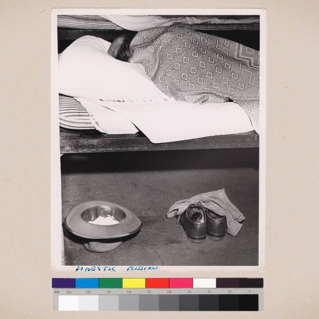 A man sleeping on a cot next to his shoes and hat on a beige background.