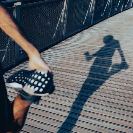 The shadow of a runner holding onto his foot to stretch before a run.