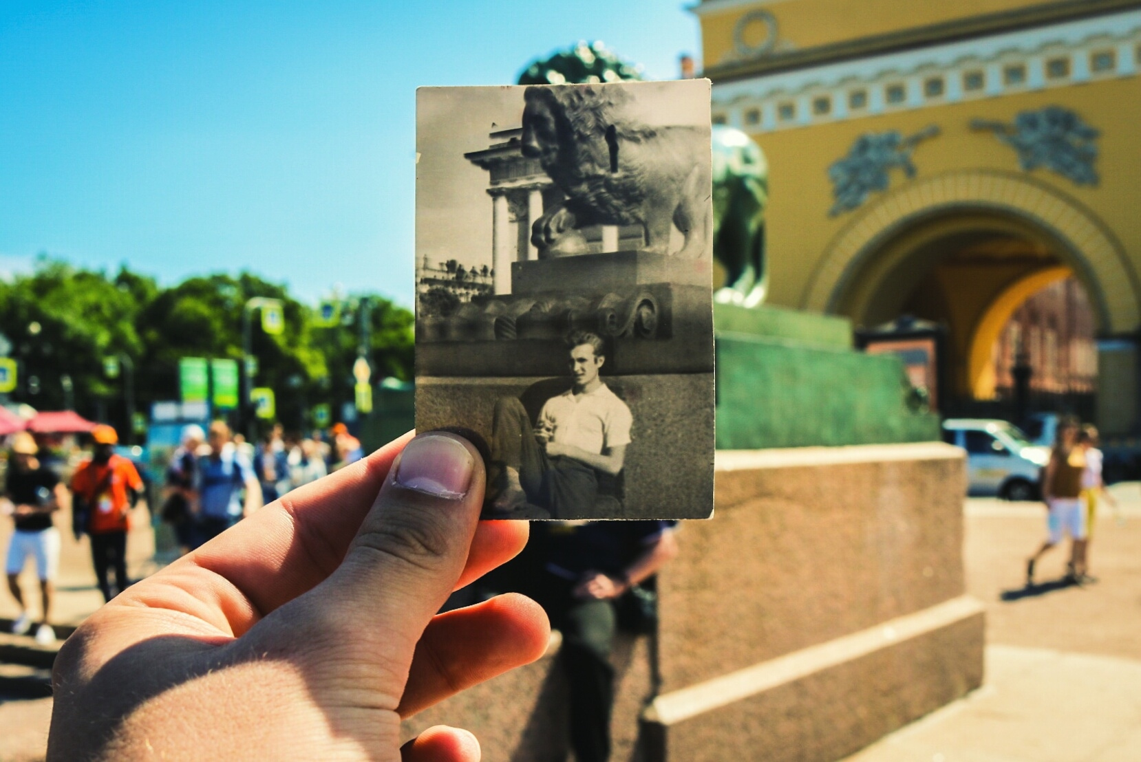 A man holding a photograph up in front of the same scene in present day.