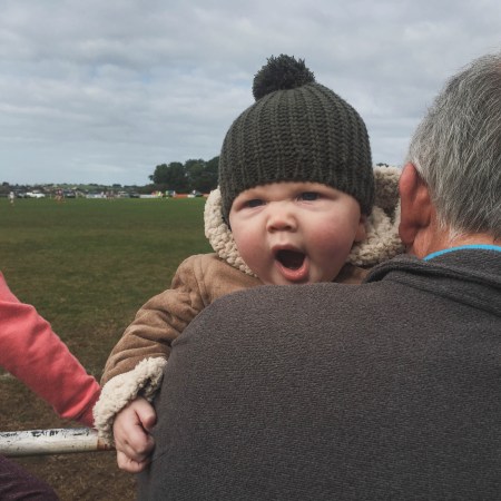 A baby yawning into the shoulder of an old man.