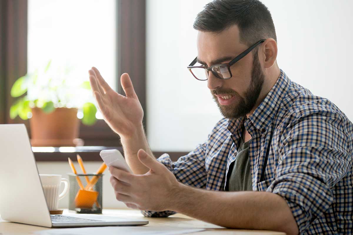 A man annoyed at a desk looking at his phone. The FCC seems poised to cut down on spam texting.