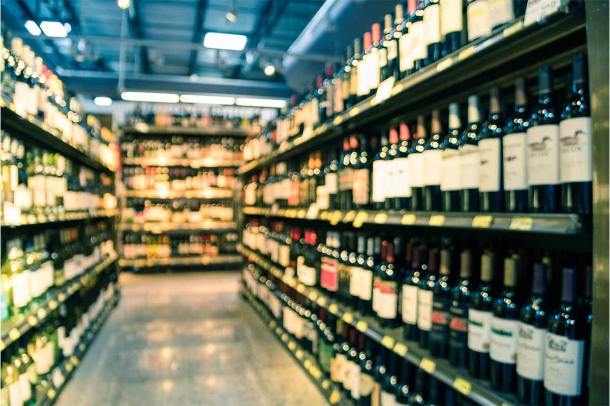 Vintage tone blurred image wine shelves with price tags on display at store in Houston, Texas, US. Defocused rows of Wine Liquor bottles on supermarket shelf. Alcoholic beverage abstract background. Wine prices haven't matched inflation in the U.S., but that's not good news for producers.