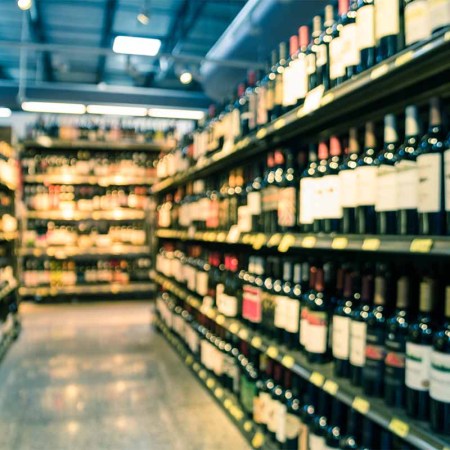 Vintage tone blurred image wine shelves with price tags on display at store in Houston, Texas, US. Defocused rows of Wine Liquor bottles on supermarket shelf. Alcoholic beverage abstract background. Wine prices haven't matched inflation in the U.S., but that's not good news for producers.