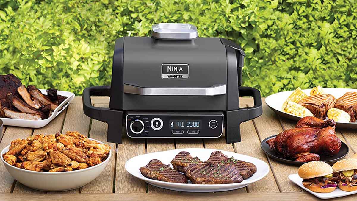 Ninja Woodfire Outdoor Grill on a table with food. The grill adds a "smoking" element to food.