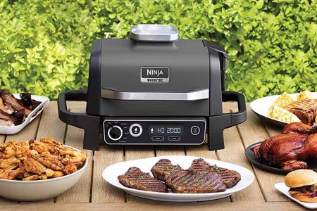 Ninja Woodfire Outdoor Grill on a table with food. The grill adds a "smoking" element to food.