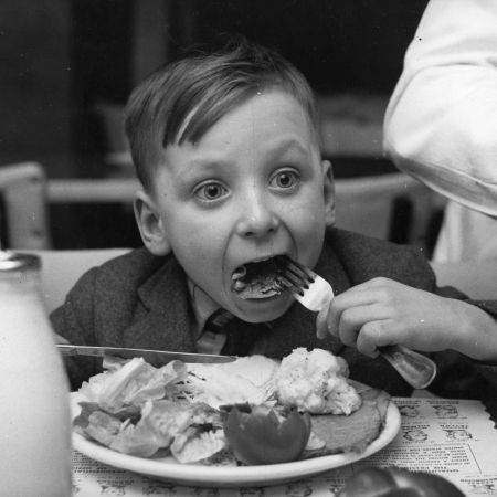 A little boy eating a plate full of food with his eyes wide.