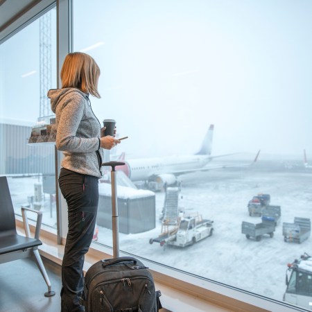 Woman standing close to a window at an airport covered in snow
