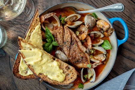 cioppino in a blue dutch oven with toasted bread and a glass of white wine