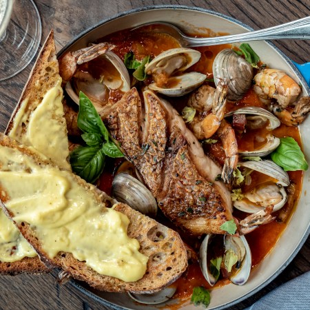 cioppino in a blue dutch oven with toasted bread and a glass of white wine