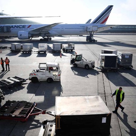 This picture taken on November 10, 2022 shows custom officials (L) monitoring as airfreight is downloaded from a Boeing 777 aircraft docked at its station at Roissy-Charles de Gaulle airport outside Paris. A new law will limit domestic flights due to CO2 emissions