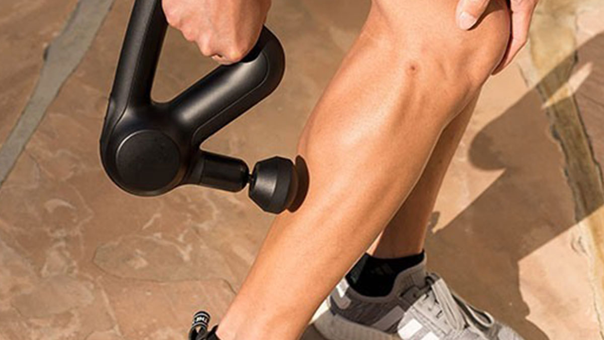 A person using a Theragun massage device on their bare leg