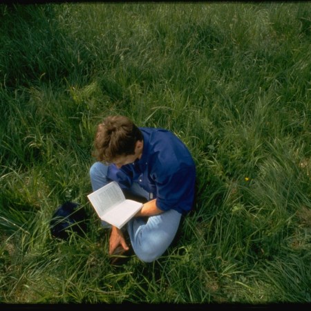 A man sitting on grass and reading a book.
