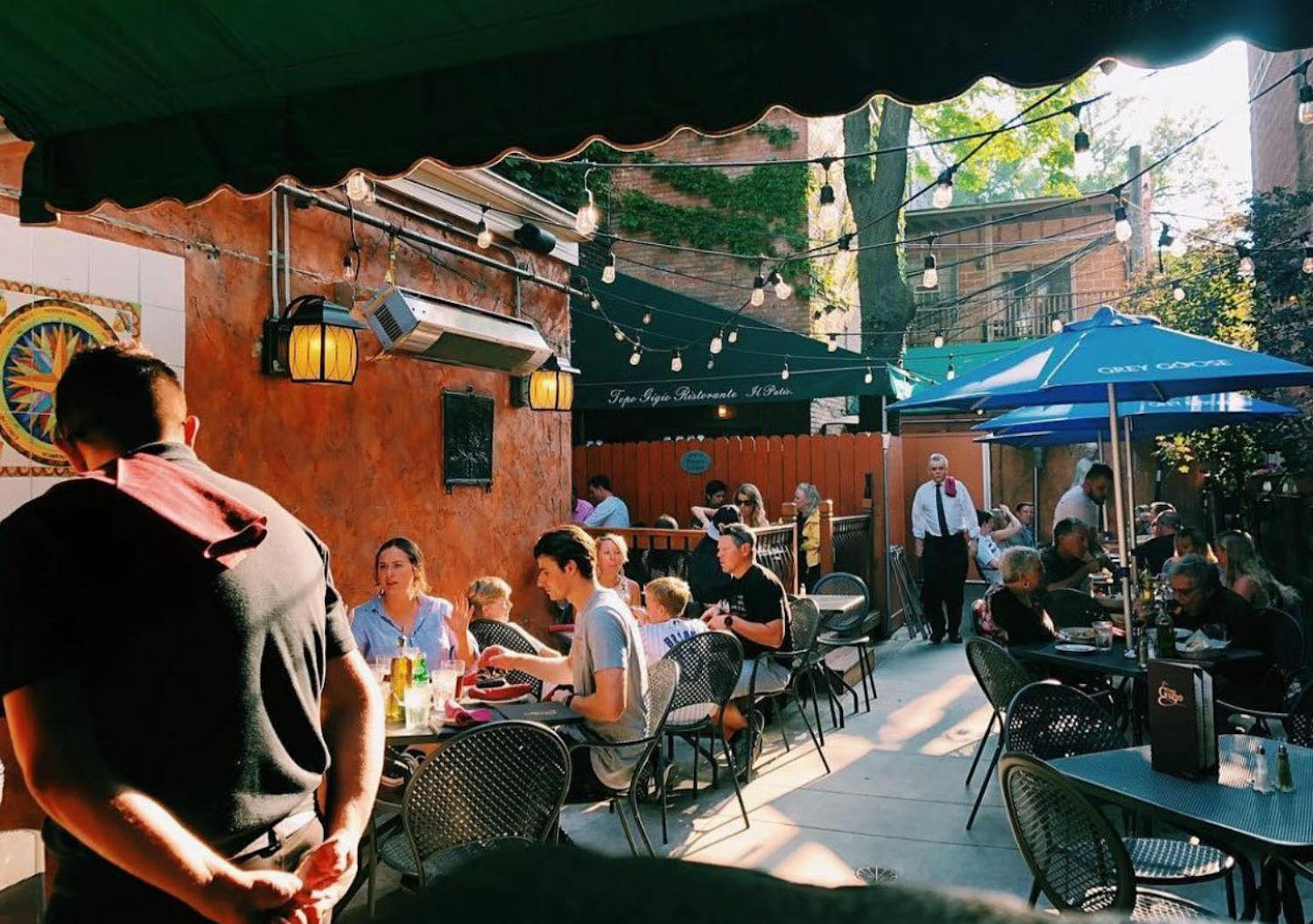 Outdoor seating area with green umbrellas, tables and string lights above