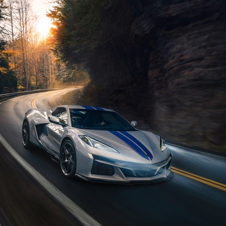 The 2024 Chevrolet Corvette E-Ray 3LZ convertible in Silver Flare with Electric Blue stripe package driving on a curved mountain road