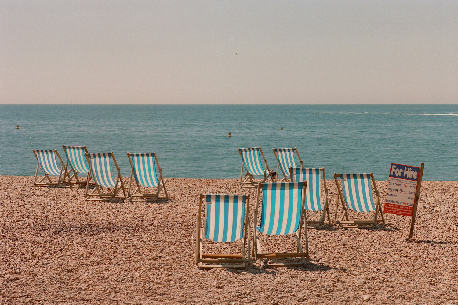 A scattering of empty pinstriped beach chairs on a rocky shoreline.