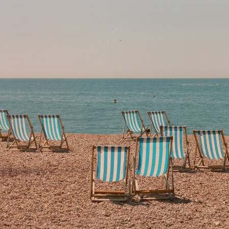 A scattering of empty pinstriped beach chairs on a rocky shoreline.