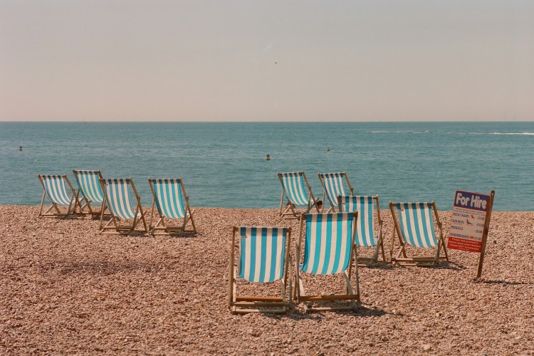 A scattering of empty pinstriped beach chairs on a rocky shoreline.