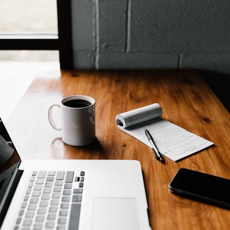 A laptop and coffee and a notepad on a table. Working out of office and/or at home is showing to be more productive for both workers and businesses.