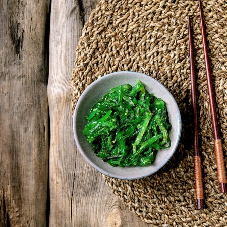 Japanese Wakame chuka seaweed salad with sesame seeds in ceramic plate with chopsticks over old wooden background