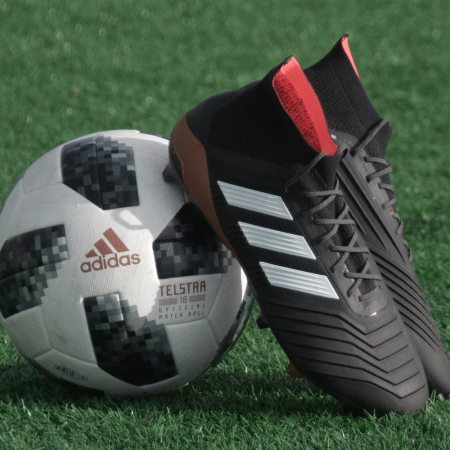 A pair of Adidas soccer cleats lean against a soccer ball.