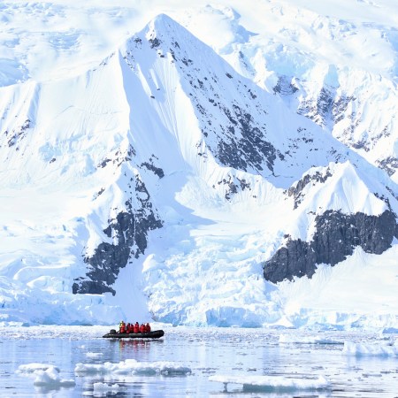 A Zodiac boat from travel company Abercrombie & Kent ferrying travelers past mountains and icebergs during an Antarctica cruise