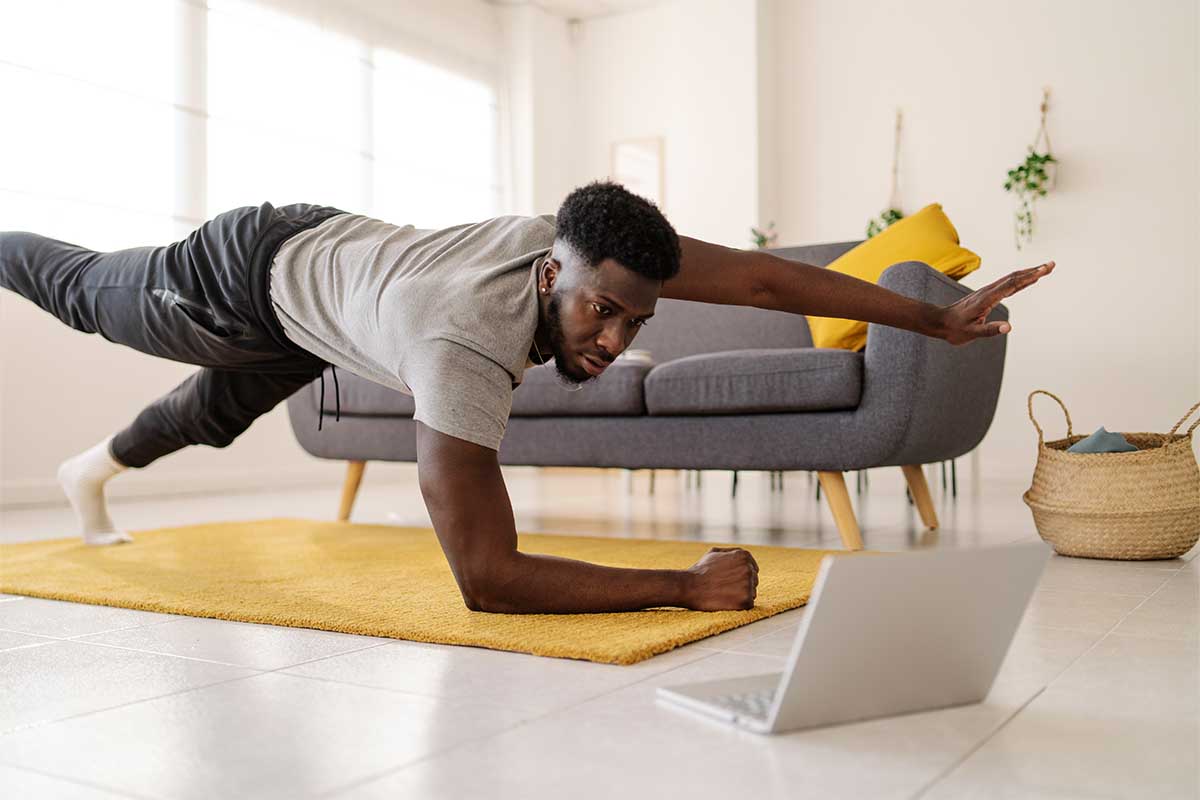 Man watching online exercise video on laptop while working out in the living room at home. ChatGPT is being used by some exercise hobbyists to create workout plans.