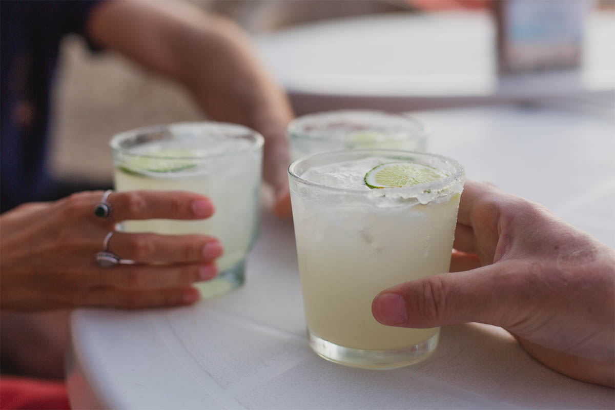 Three people (hands only) holding three full margaritas on a table. According to a new economic report by DISCUS, spirits sales (helped by tequila) just passed beer sales in the U.S.