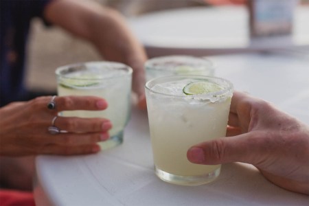 Three people (hands only) holding three full margaritas on a table. According to a new economic report by DISCUS, spirits sales (helped by tequila) just passed beer sales in the U.S.
