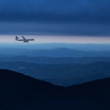 Commercial airplane flying above mountain ranges in cloudy sky at night.