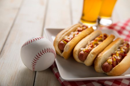 Three hot dogs on a white plate on a white wooden picnic bench
