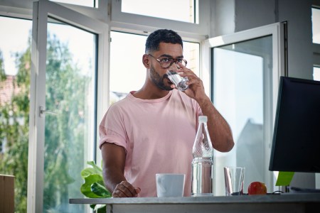 man in a pink tee shirt and glasses drinking water