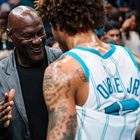 Michael Jordan, owner of the Charlotte Hornets, goes in for a handshake with one of his team's players on the sidelines of a basketball court