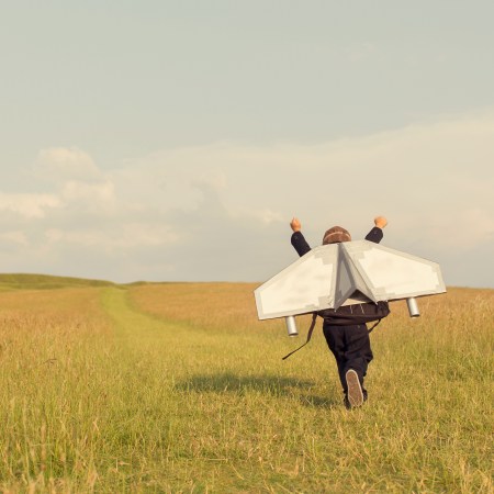 A kid running through a field with an arts and crafts jetpack on his back.