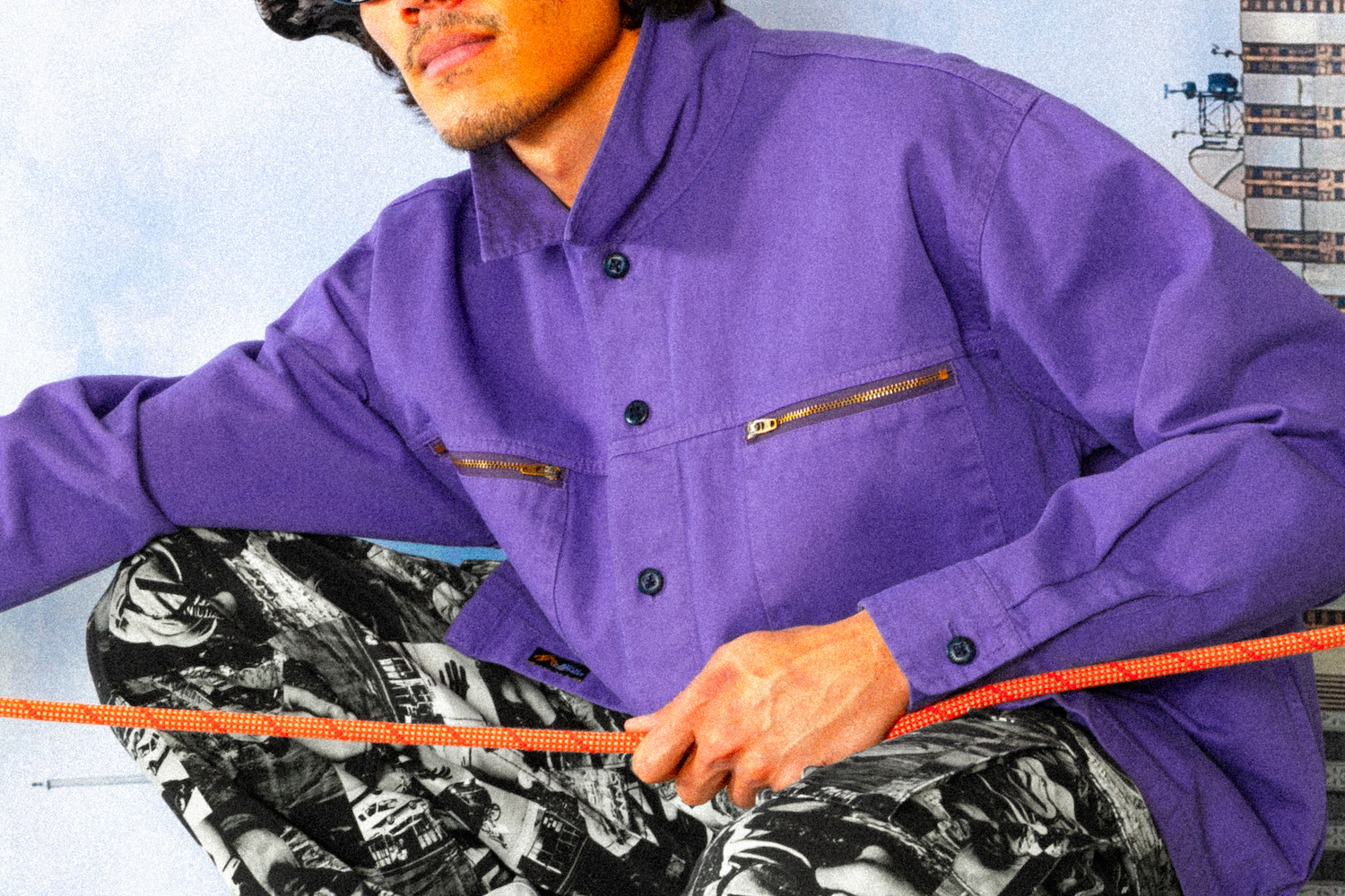 a model in a pruple overshirt holding onto an orange climbing rope